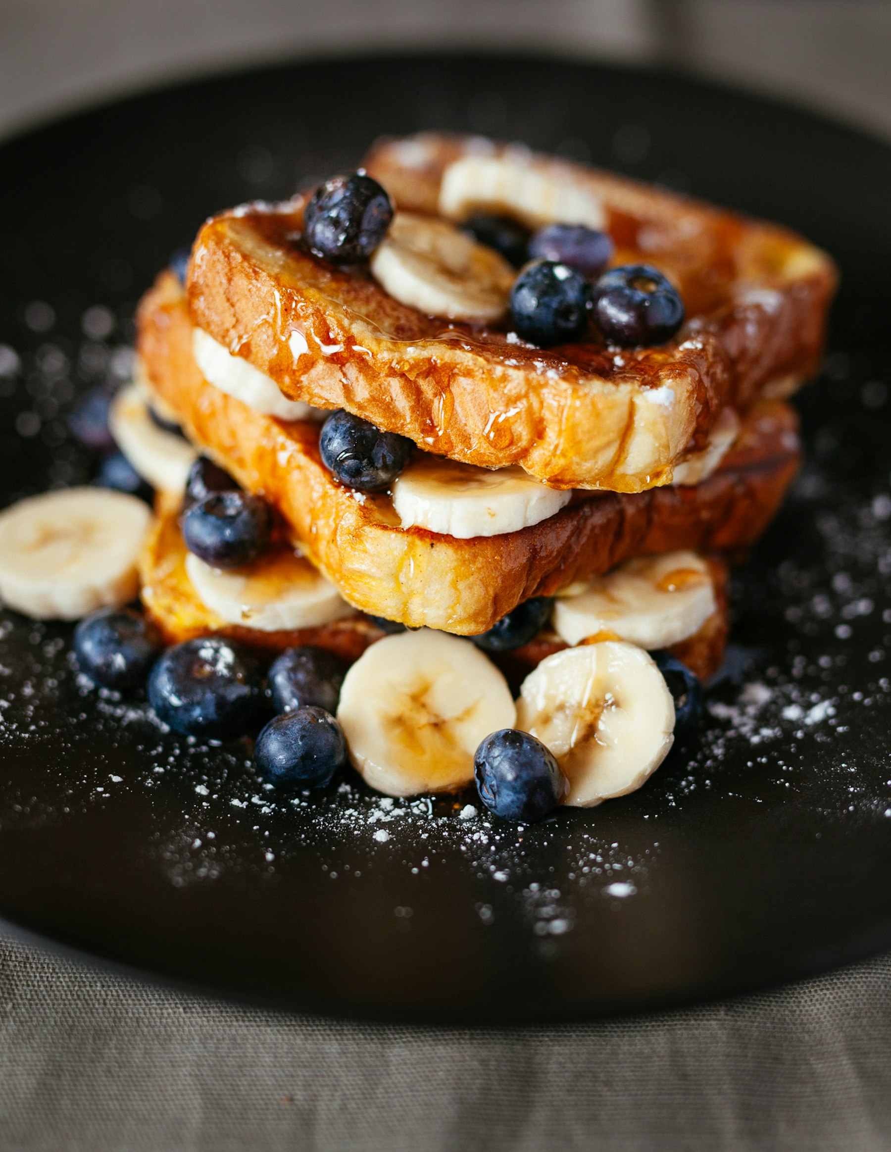 A golden breakfast stack with banana, blueberries and icing sugar